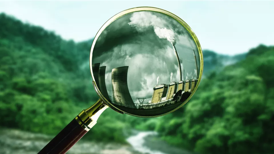 A magnifying held towards greenary but shows industry polluting air. Photo montage.