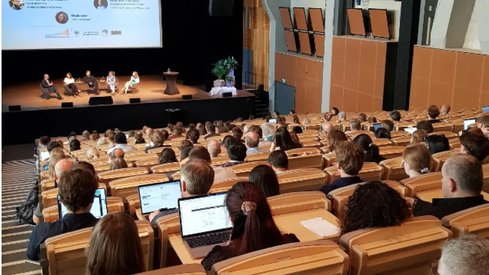 A large audience listening to a panel sitting on a stage