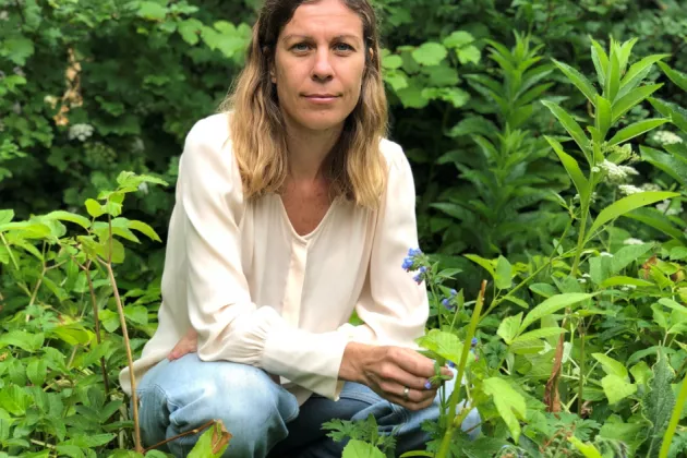 Woman in a white shirt sitting among green. Photo.