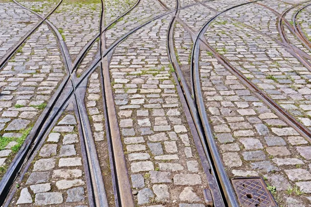 Railway lines crossing on cobbled stone ground, grass inbetween. Photo.