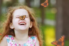 A girl is laughing. A butterfly sits on her nose.